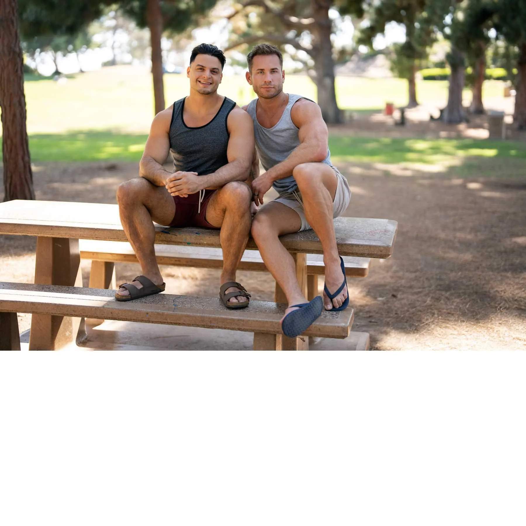 Two clothed males posed seated on picnic table
