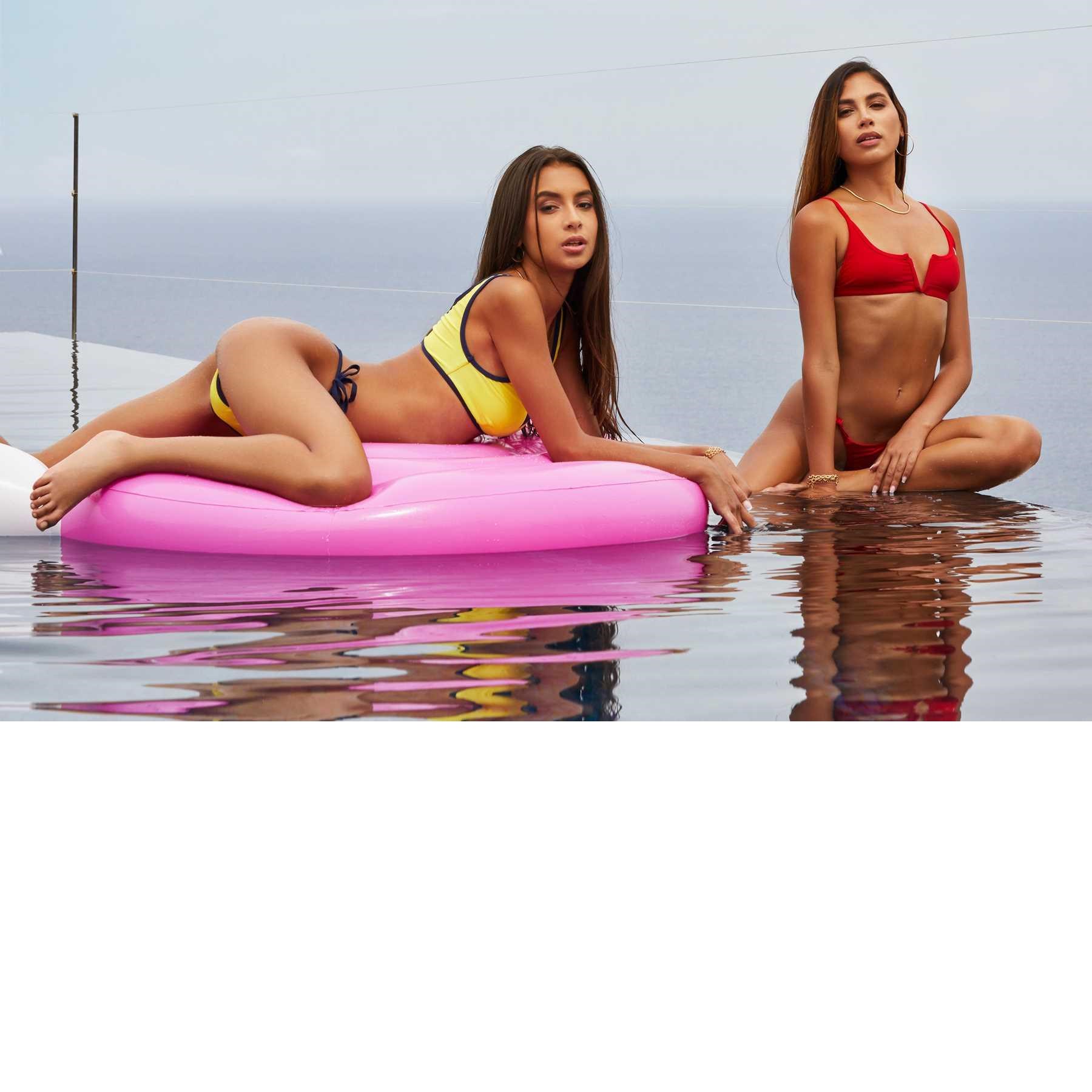 Two brunette females wearing bikinis in water one on raft