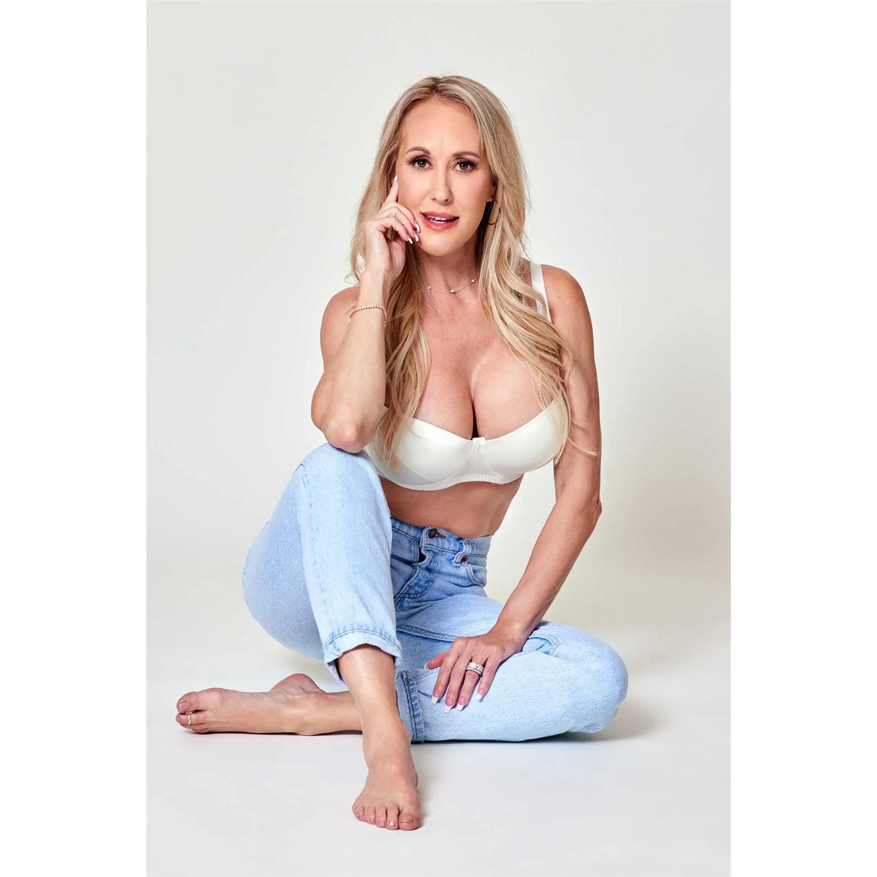 Blonde posed seated wearing bra and jeans displaying breasts