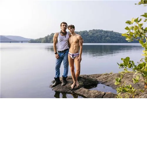 Male wearing briefs caressing clothed male outdoors